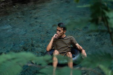 Bir adam yüzen bir tüp kullanarak çok temiz bir bahar nehrinden zevk alır. Udal Gumuk nehri, Magelang, Orta Java, Endonezya.