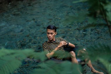 Bir adam yüzen bir tüp kullanarak çok temiz bir bahar nehrinden zevk alır. Udal Gumuk nehri, Magelang, Orta Java, Endonezya.