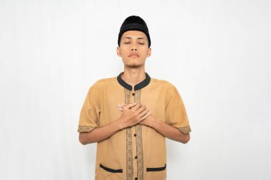 Müslüman kıyafeti giyen Asyalı Müslüman adam ya dua ediyor ya da gönlünü ferahlatıyor. İzole edilmiş beyaz arkaplan.