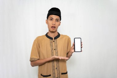 Zeki telefon ekranını işaret ederken gülümseyen kahverengi Müslüman kılıklı Asyalı bir adam. İzole edilmiş beyaz arkaplan.