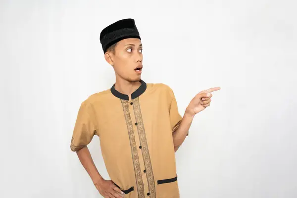 stock image Asian Muslim man wearing brown Muslim clothes smiling happily while pointing at an empty space. Isolated white background.