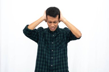 Yeşil kareli bir gömlek giyen Asyalı bir adam başını tutuyor ve yüksek seviyede stres ve çığlık atıyor. İzole edilmiş beyaz arkaplan.