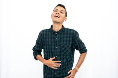 Yeşil kareli bir gömlek giyen Asyalı bir adam karnını tutarken rahatlama ya da mide ağrısı çekiyor. İzole edilmiş beyaz arkaplan.