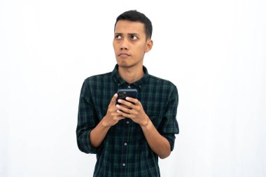 Yeşil kareli günlük gömlek giyen Asyalı adam akıllı telefon tutarken düşünüyor. İzole edilmiş beyaz arkaplan.