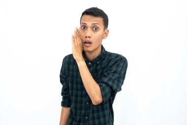Asyalı bir adam kulağına fısıldarken elleri ağzının yanında olan yeşil kareli bir gömlek giyiyor. İzole edilmiş beyaz arkaplan.