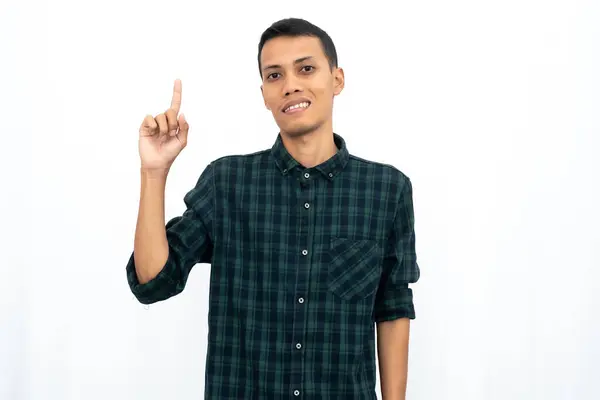 stock image Asian man wearing a green checkered casual shirt pointing towards an empty space for advertising. Isolated white background.