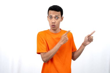Portakal rengi tişört giyen genç bir Asyalı 'nın portresi promosyon alanı için fotokopi alanını işaret ediyor. beyaz arkaplanda izole.