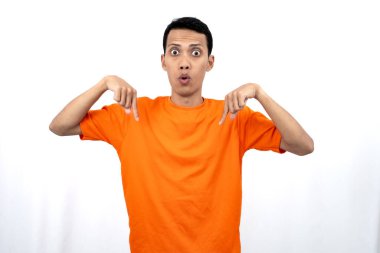 Portakal rengi tişört giyen genç bir Asyalı 'nın portresi promosyon alanı için fotokopi alanını işaret ediyor. beyaz arkaplanda izole.
