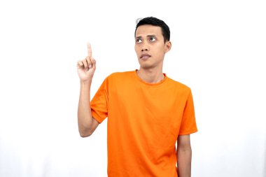 Portakal rengi tişört giyen genç bir Asyalı 'nın portresi promosyon alanı için fotokopi alanını işaret ediyor. beyaz arkaplanda izole.