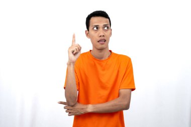 Portakal rengi tişört giyen genç bir Asyalı 'nın portresi promosyon alanı için fotokopi alanını işaret ediyor. beyaz arkaplanda izole.