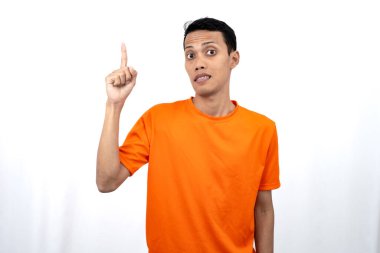 Portakal rengi tişört giyen genç bir Asyalı 'nın portresi promosyon alanı için fotokopi alanını işaret ediyor. beyaz arkaplanda izole.