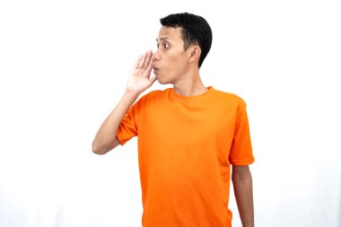 Elleri ağzının kenarında turuncu tişört giyen genç Asyalı bir adamın portresi. Dedikoduları fısıldıyor ve sırlarını anlatıyor. Beyaz arka planda izole edilmiş haberleri paylaşıyorlar..