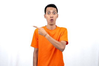 Portakal rengi tişört giyen genç bir Asyalı 'nın portresi promosyon alanı için fotokopi alanını işaret ediyor. beyaz arkaplanda izole.