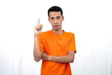 Portakal rengi tişört giyen genç bir Asyalı 'nın portresi promosyon alanı için fotokopi alanını işaret ediyor. beyaz arkaplanda izole.
