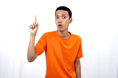 Portakal rengi tişört giyen genç bir Asyalı 'nın portresi promosyon alanı için fotokopi alanını işaret ediyor. beyaz arkaplanda izole.