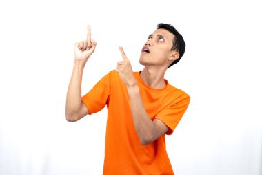 Portakal rengi tişört giyen genç bir Asyalı 'nın portresi promosyon alanı için fotokopi alanını işaret ediyor. beyaz arkaplanda izole.