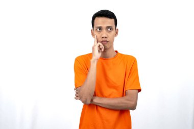 Turuncu tişört giyen, düşünen, fikir arayan ya da kafası karışmış Asyalı genç bir adamın portresi. Beyaz arkaplanda izole.