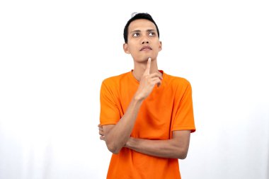 Turuncu tişört giyen, düşünen, fikir arayan ya da kafası karışmış Asyalı genç bir adamın portresi. Beyaz arkaplanda izole.