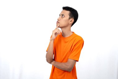 Turuncu tişört giyen, düşünen, fikir arayan ya da kafası karışmış Asyalı genç bir adamın portresi. Beyaz arkaplanda izole.