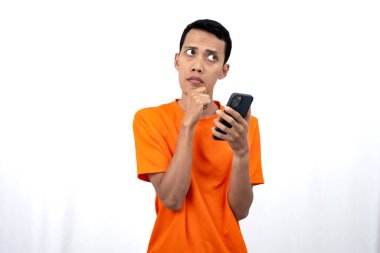 Turuncu tişört giyen genç bir Asyalı 'nın portresi akıllı telefon tutarken düşündüğünü gösteriyor. Beyaz arkaplanda izole.