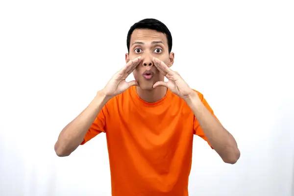 stock image Portrait of a young Asian man wearing an orange t-shirt with his hand near his mouth whispering gossip and telling secrets while sharing news isolated on white background.