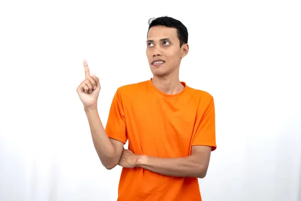 Portakal rengi tişört giyen genç bir Asyalı 'nın portresi promosyon alanı için fotokopi alanını işaret ediyor. beyaz arkaplanda izole.