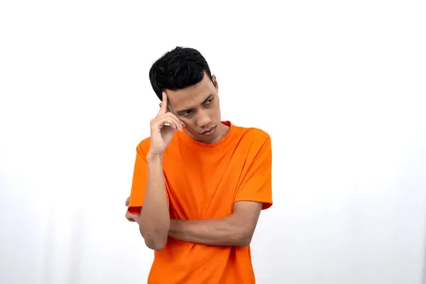 stock image Portrait of a young Asian man wearing an orange t-shirt posing thinking, searching for ideas, or confused. Isolated on white background.