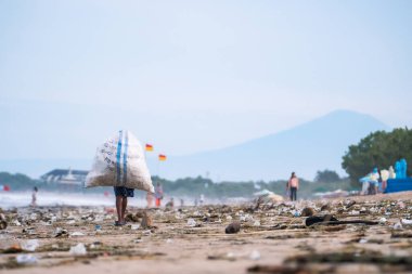 Bali, Endonezya - 09 Mart 2024: Bali 'deki çok kirli Kuta Sahili' nde çöp torbaları taşıyan leş yiyiciler. Hala kullanılabilen kullanılmış çöp aranıyor.