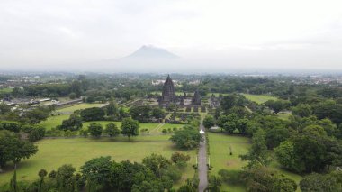 Morning aerial view of the Prambanan temple area in Yogyakarta, with the majestic Mount Merapi clearly visible in the background. clipart