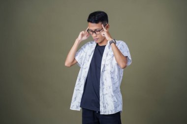 Gözlüklü, beyaz gömlekli, düşünceli, başı dönen ya da fikir arayan Asyalı bir adam. Ordu yeşil arka planında izole edilmiş..