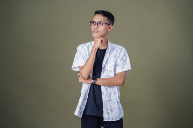 Gözlüklü, beyaz gömlekli, düşünceli, başı dönen ya da fikir arayan Asyalı bir adam. Ordu yeşil arka planında izole edilmiş..