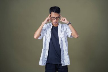 Gözlüklü, beyaz gömlekli, düşünceli, başı dönen ya da fikir arayan Asyalı bir adam. Ordu yeşil arka planında izole edilmiş..