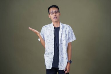 Heyecanlı, şok olmuş ya da heyecanlı bir poz. Boş uzayın kenarını gösteren el işaretleriyle bağırıyorlar. Gözlüklü, sıradan beyaz tişörtlü Asyalı bir adam askeri yeşil arka planda izole edilmiş..