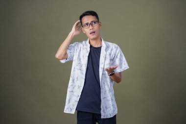 Gözlüklü, beyaz gömlekli, düşünceli, başı dönen ya da fikir arayan Asyalı bir adam. Ordu yeşil arka planında izole edilmiş..