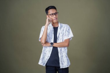 Gözlüklü, beyaz gömlekli, düşünceli, başı dönen ya da fikir arayan Asyalı bir adam. Ordu yeşil arka planında izole edilmiş..