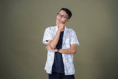 Gözlüklü, beyaz gömlekli, düşünceli, başı dönen ya da fikir arayan Asyalı bir adam. Ordu yeşil arka planında izole edilmiş..