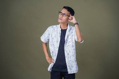 Gözlüklü, beyaz gömlekli, düşünceli, başı dönen ya da fikir arayan Asyalı bir adam. Ordu yeşil arka planında izole edilmiş..