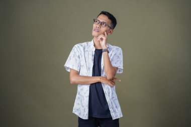 Gözlüklü, beyaz gömlekli, düşünceli, başı dönen ya da fikir arayan Asyalı bir adam. Ordu yeşil arka planında izole edilmiş..