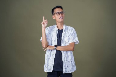 Gözlüklü, beyaz gömlekli, düşünceli, başı dönen ya da fikir arayan Asyalı bir adam. Ordu yeşil arka planında izole edilmiş..