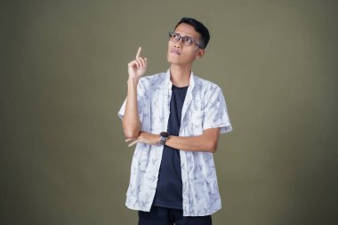 Gözlüklü, beyaz gömlekli, düşünceli, başı dönen ya da fikir arayan Asyalı bir adam. Ordu yeşil arka planında izole edilmiş..