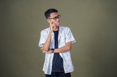 Gözlüklü, beyaz gömlekli, düşünceli, başı dönen ya da fikir arayan Asyalı bir adam. Ordu yeşil arka planında izole edilmiş..