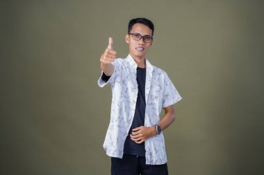 Gözlüklü, beyaz gömlekli, Asyalı bir adam. Mutlu bir şekilde baş parmak hareketi yapmak. Ordu yeşil arka planında izole edilmiş..