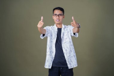 Gözlüklü, beyaz gömlekli, Asyalı bir adam. Mutlu bir şekilde baş parmak hareketi yapmak. Ordu yeşil arka planında izole edilmiş..