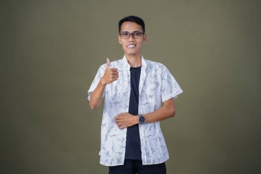 Gözlüklü, beyaz gömlekli, Asyalı bir adam. Mutlu bir şekilde baş parmak hareketi yapmak. Ordu yeşil arka planında izole edilmiş..