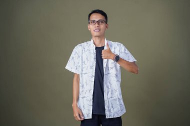 Gözlüklü, beyaz gömlekli, Asyalı bir adam. Mutlu bir şekilde baş parmak hareketi yapmak. Ordu yeşil arka planında izole edilmiş..