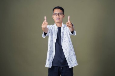 Gözlüklü, beyaz gömlekli, Asyalı bir adam. Mutlu bir şekilde baş parmak hareketi yapmak. Ordu yeşil arka planında izole edilmiş..
