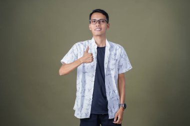 Gözlüklü, beyaz gömlekli, Asyalı bir adam. Mutlu bir şekilde baş parmak hareketi yapmak. Ordu yeşil arka planında izole edilmiş..