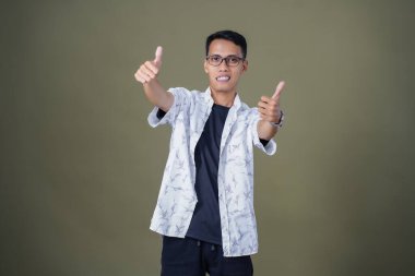 Gözlüklü, beyaz gömlekli, Asyalı bir adam. Mutlu bir şekilde baş parmak hareketi yapmak. Ordu yeşil arka planında izole edilmiş..