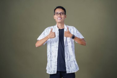 Gözlüklü, beyaz gömlekli, Asyalı bir adam. Mutlu bir şekilde baş parmak hareketi yapmak. Ordu yeşil arka planında izole edilmiş..