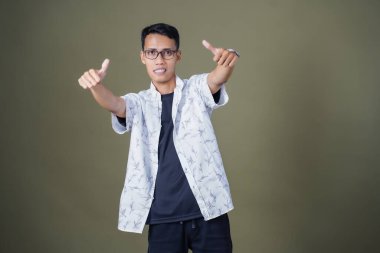 Gözlüklü, beyaz gömlekli, Asyalı bir adam. Mutlu bir şekilde baş parmak hareketi yapmak. Ordu yeşil arka planında izole edilmiş..